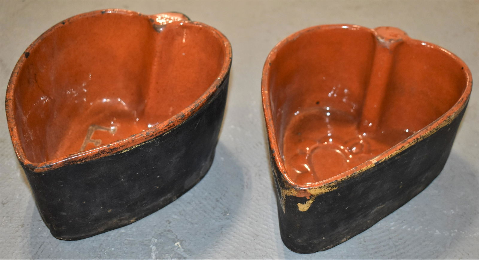 (2) Heart Shaped Redware Molds: (2) 19TH CENTURY GLAZED REDWARE HEART SHAPED MOLDS WITH HANDLES - (1) W/ RAISED INTERIOR DESIGN AND (1) W/ SLIP DECORATED YELLOW INITIALS F. E. ON BOTTOM INTERIOR - PROBABLY CONTINENTAL - 8 1/2"L X 5