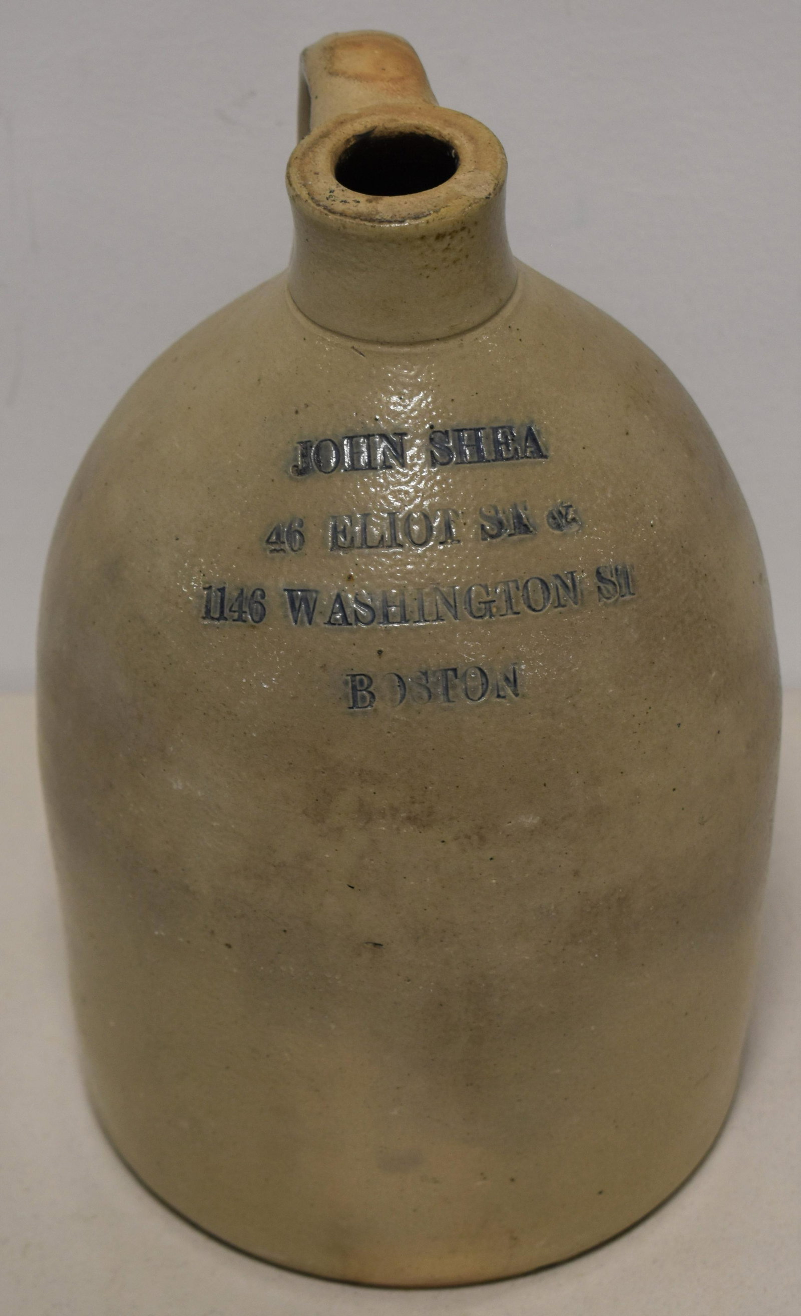 1 Gallon Stoneware Advertising Jug: 11 1/2 GREY STONEWARE JUG IMPRESSED STAMP FOR JOHN SHEA 46 ELLIOT STREET AND 1146 WASHINGTON STREET BOSTON HIGHLIGHTED IN BLUE - SMALL TOP RIM NICK, WEAR, AND DISCOLORATION