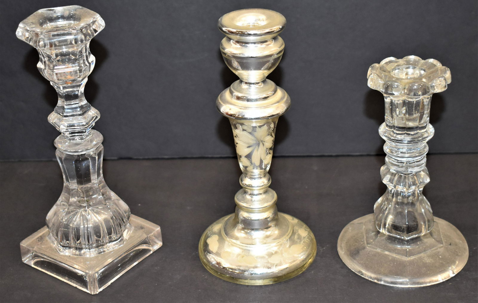 (3) Early Glass Candlesticks: LOT (3) EARLY GLASS CANDLESTICKS - (1) 51/2" CLEAR SANDWICH CANDLESTICKS - (1) 7 1/4" CLEAR SANDWICH CANDLE STICK AND (1) 7 1/2" DECORATED MERCURY GLASS CANDLE STICK - WEAR AND IMPERFECTIONS