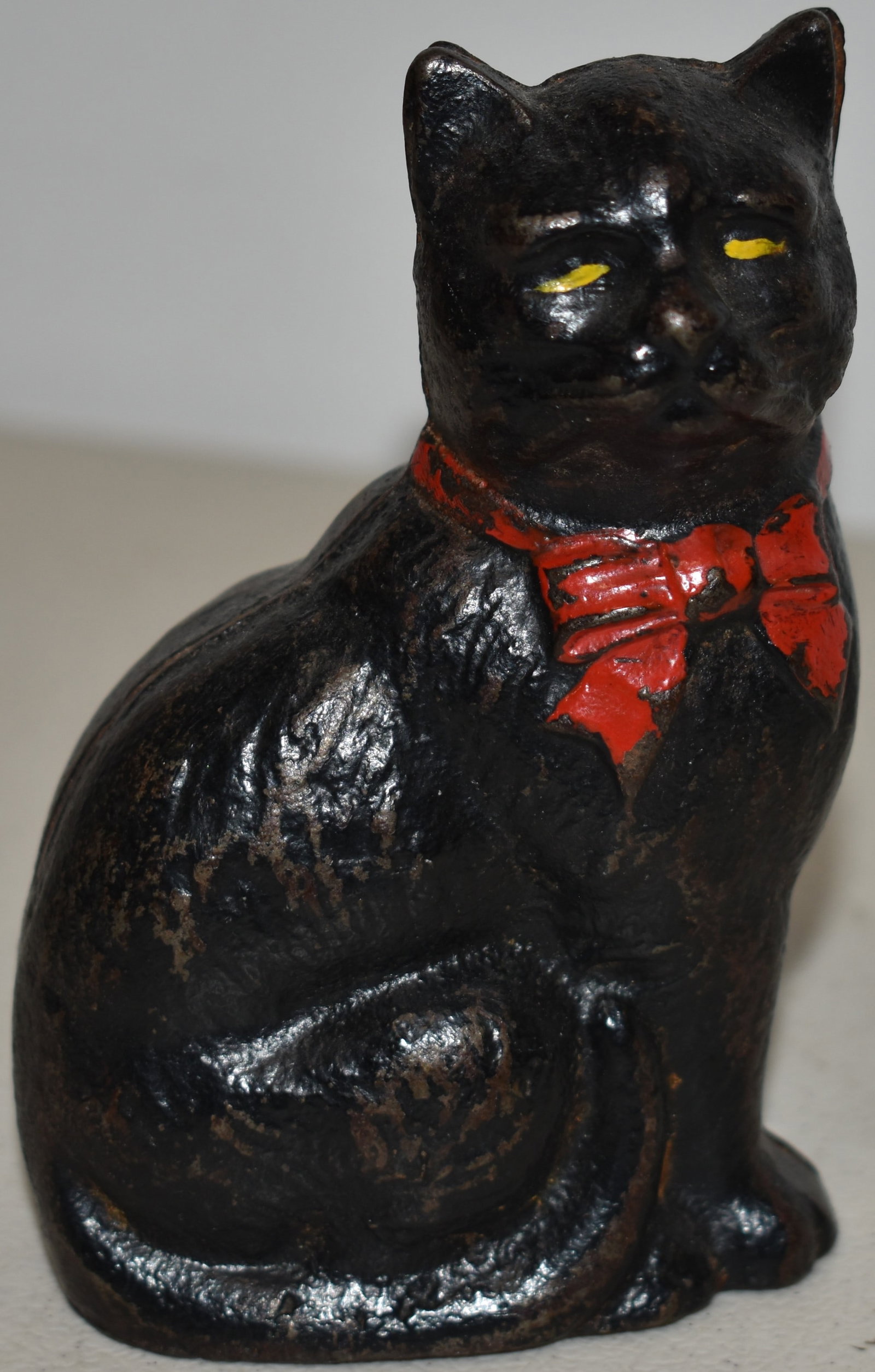 CAST IRON SEATED CAT STILL BANK: VINTAGE PAINTED SEATED CAT W/ RED RIBBON STILL BANK - 2 3/4" L X 4 1/4" T - WEAR