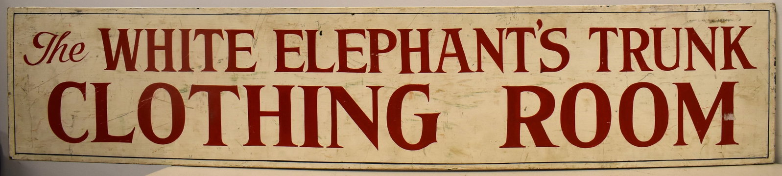 VINTAGE PAINTED WOODEN TRADE SIGN: MID 20TH CENT PAINTED TRADE SIGN - " THE WHITE ELEPHANTS TRUNK" - CLOTHING ROOM - 44" L X 9 1/4" W - SINGLE SIDED - WEAR & IMPERFECTIONS