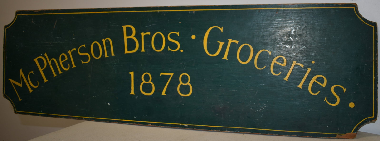 VITNAGE PAINTED WOODEN TRADE SIGN: MID 20TH CENT PAINTED WOODEN TRADE SIGN FOR MCPHERSON BROS. GROCERIES 1878 - GREEN W/ WHITE LETTERING - 36" X 11" SINGLE SIDED - WEAR, SM. EDGE LOSSES & IMPERFECTIONS