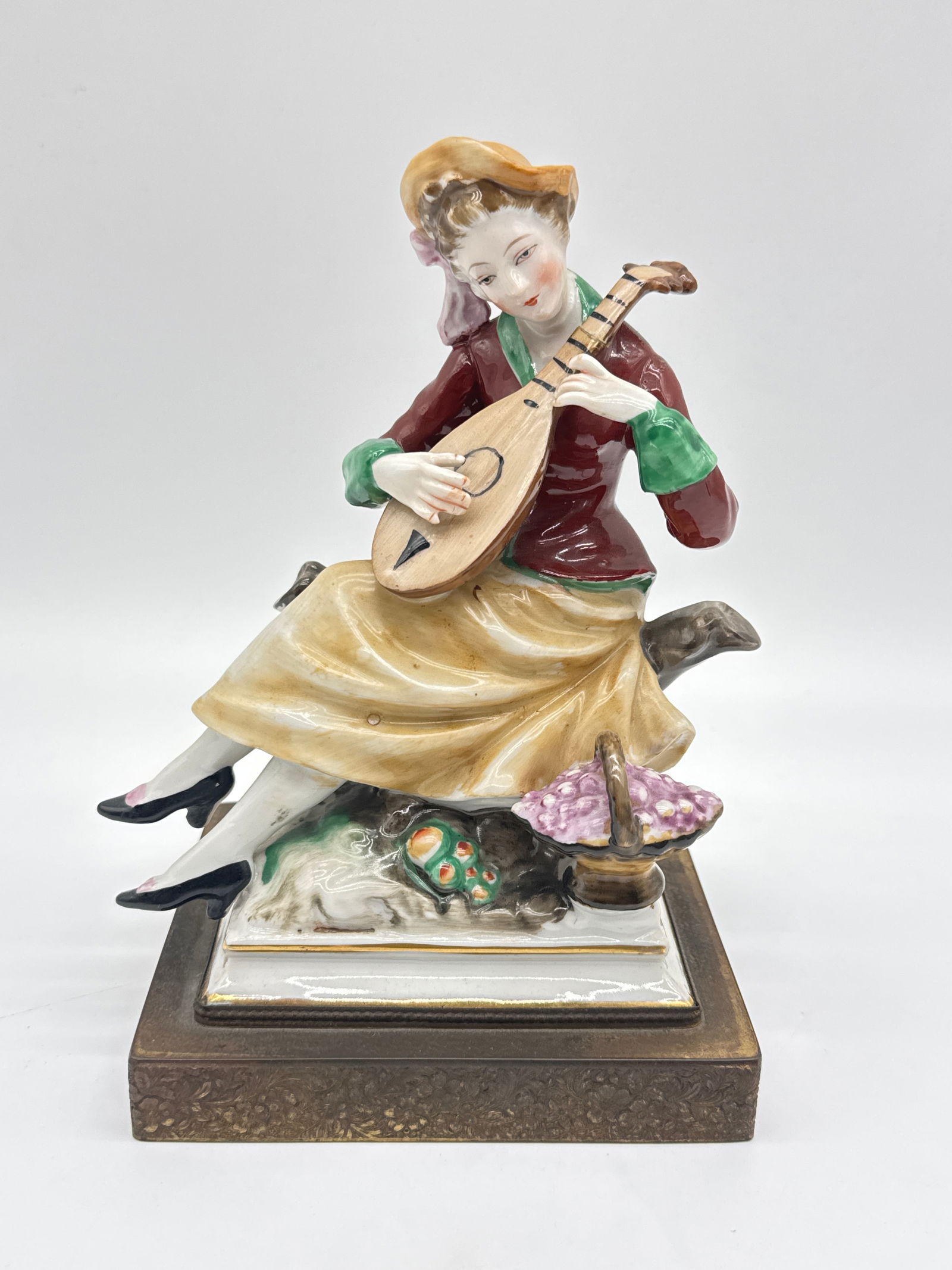 Charming Vintage Porcelain Figurine of Woman with Mandolin – 8” Tall (090 white): Serenade your shelf with this enchanting vintage porcelain figurine, capturing a graceful woman in a wide-brimmed hat, mid-strum on a mandolin. Dressed in a crimson jacket and golden skirt, she sits d