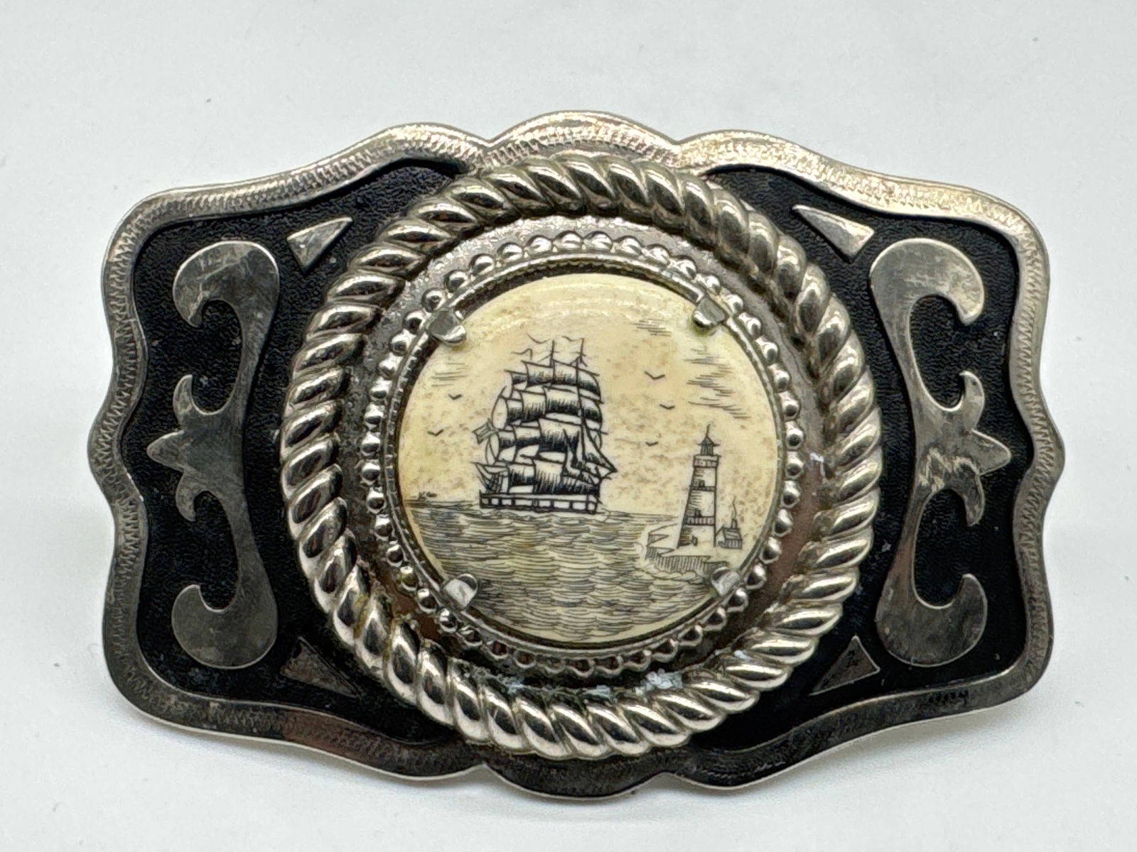 VTG Nautical Scrimshaw-Style Belt Buckle–Tall Ship & Lighthouse Scene, Faux Bone? (185 white Adam): Ahoy, collectors and free spirits! This vintage belt buckle is pure maritime magic. At its center is a detailed scrimshaw-style scene featuring a majestic tall ship sailing past a lighthouse—etched