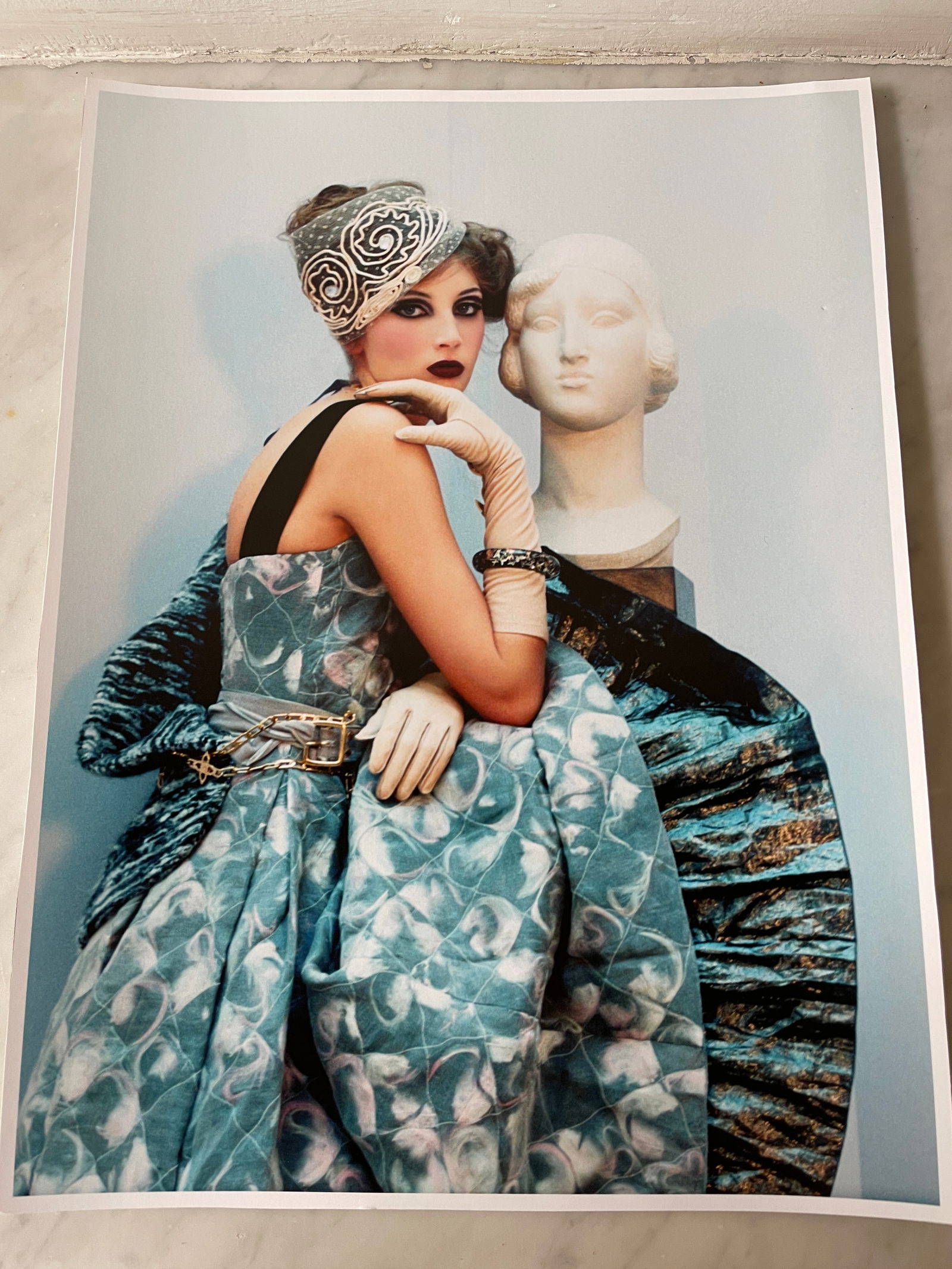 Irina Ionesco (1930–2022) – Woman with an Antique Bust. Color photograph featuring a woman: Irina Ionesco (1930–2022) – Woman with an Antique Bust. Color photograph featuring a woman elegantly dressed in a sumptuous blue-green dress with an abstract pattern, belted at the waist and acces