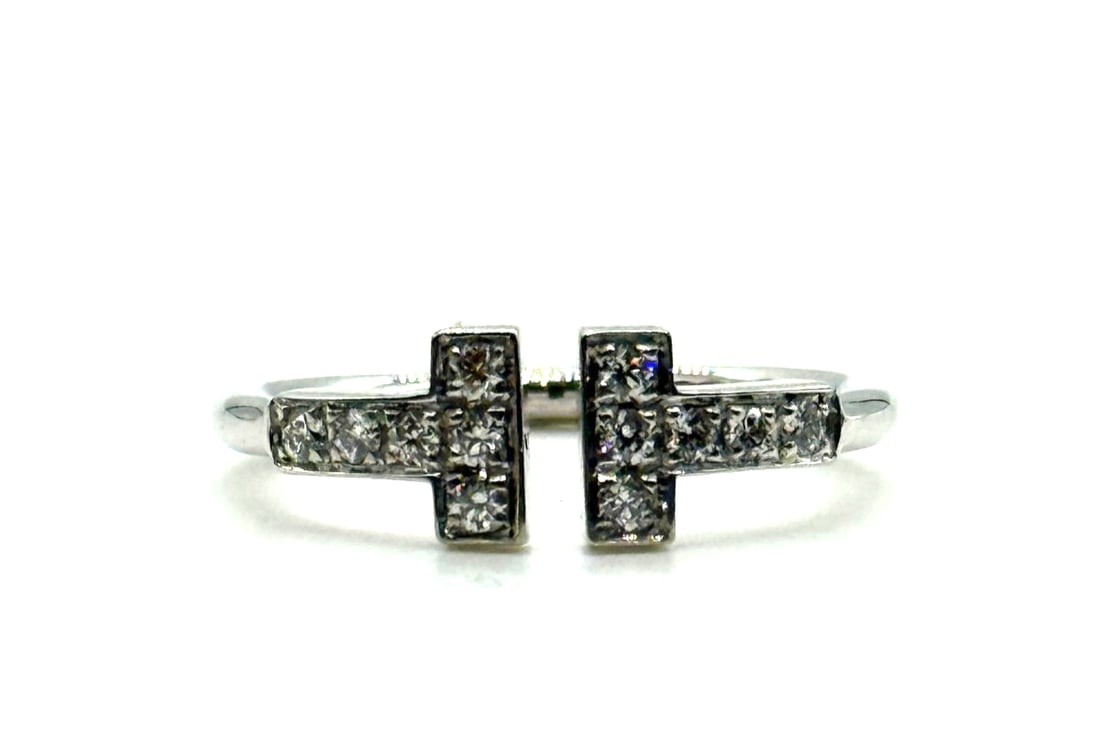 Tiffany & Co. T Wire Ring 18K White Gold with Diamonds: The Tiffany & Co. T Wire Ring is a luxurious piece of fine jewelry crafted from 18K white gold with a pavé setting style. The main stone is a round brilliant diamond with excellent cut grading and ve