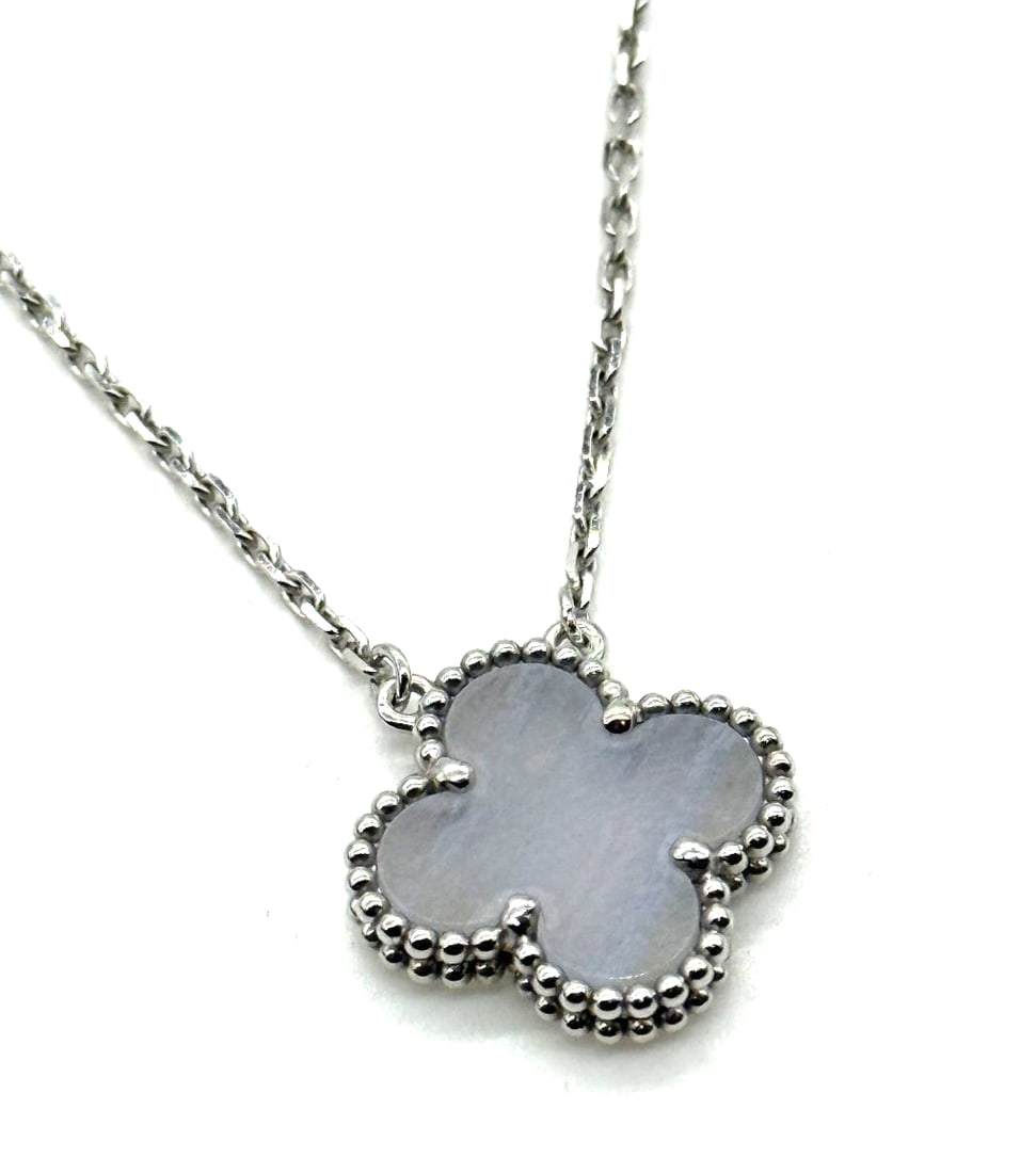 Van Cleef & Arpels Vintage Alhambra 18KT White Gold Necklace Chalcedony: The Van Cleef & Arpels Vintage Alhambra 18KT White Gold Necklace with Chalcedony features a clover-shaped pendant adorned with blue chalcedony stones. This elegant necklace has a lobster closure and i