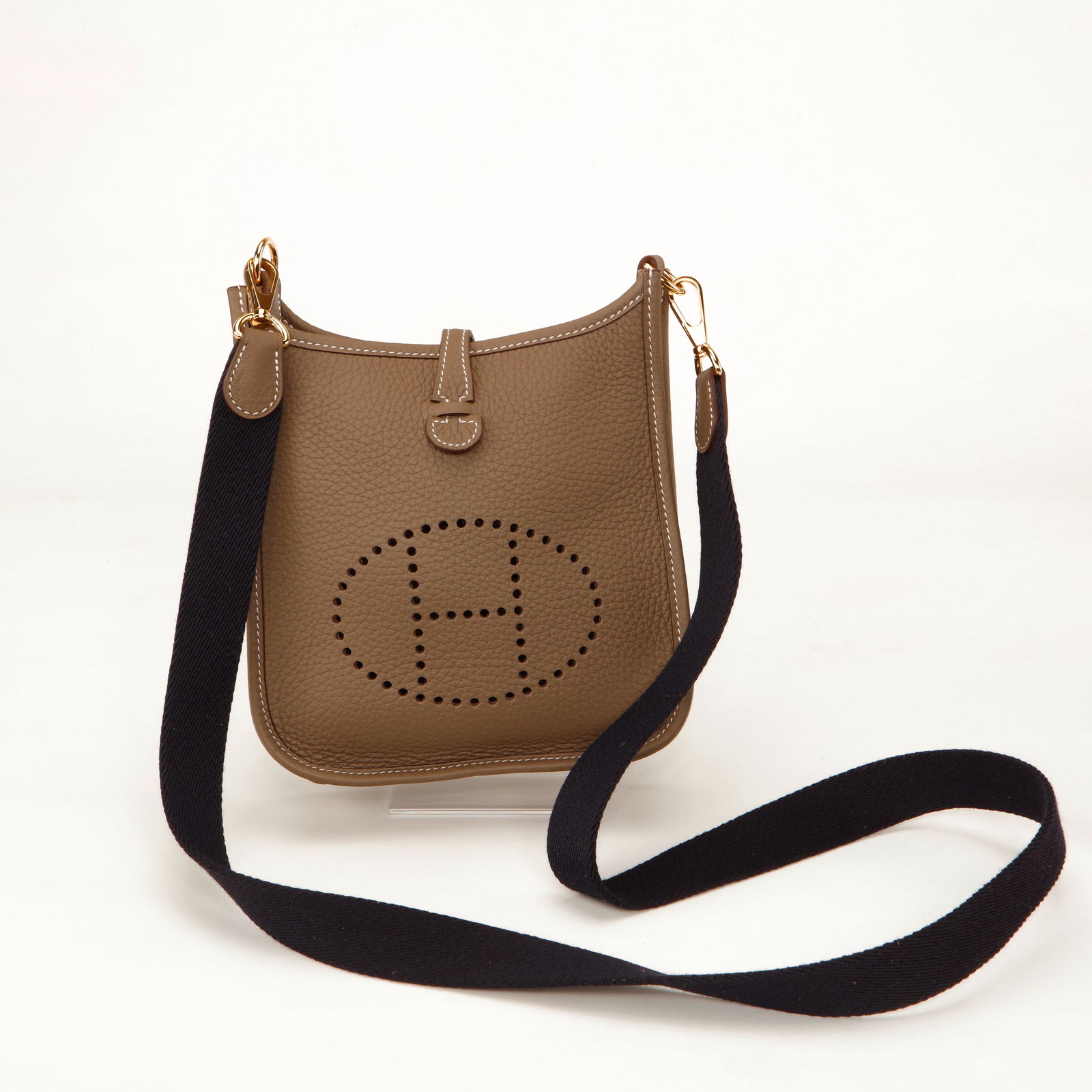 Hermès Evelyne TPM Clemence Leather Crossbody Bag – Etoupe with Gold Hardware: Authentic Hermès Evelyne TPM crafted in grained Clemence leather in the timeless Etoupe shade. Featuring the iconic perforated “H” logo on the front, contrast white stitching, and elegant gol