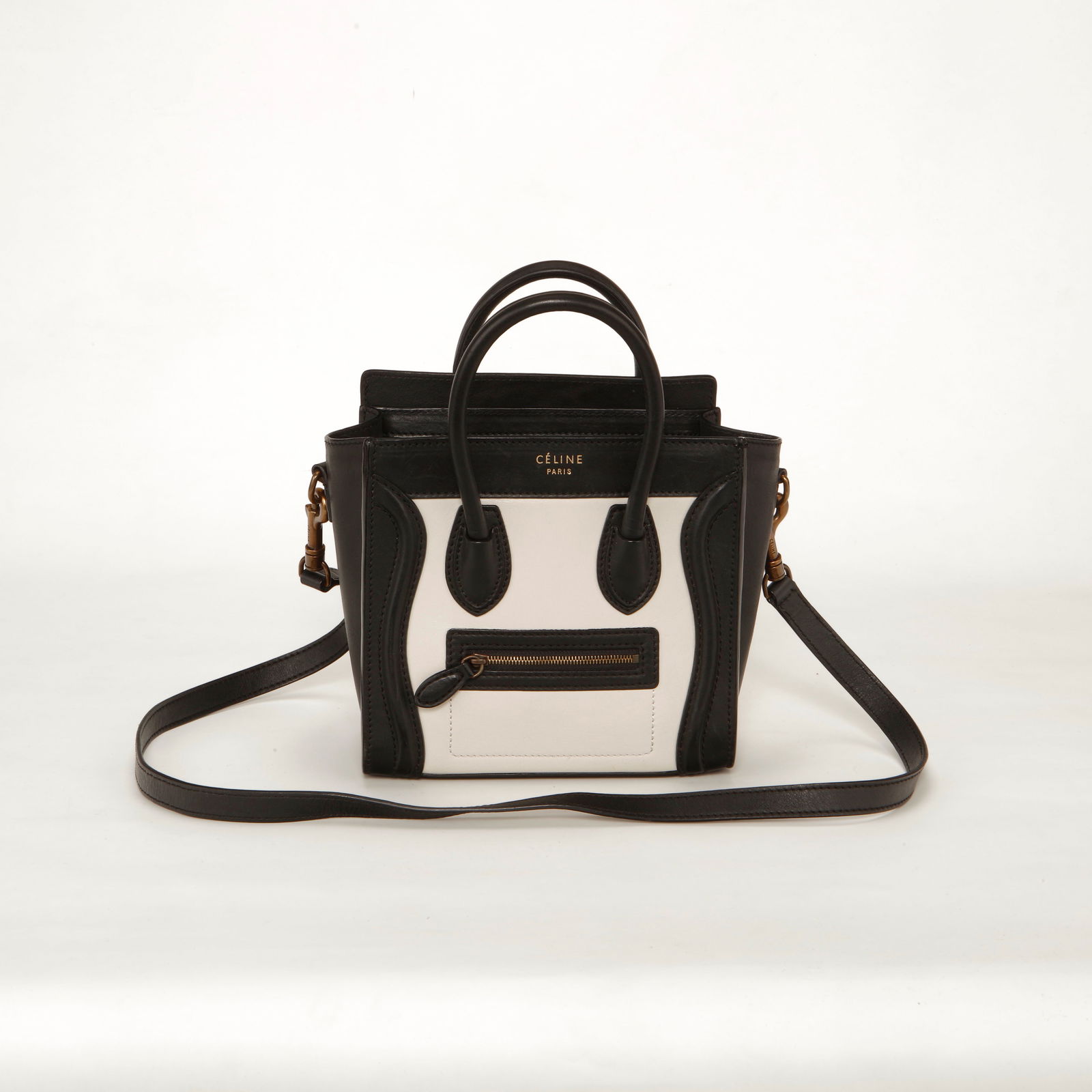 Celine Nano Luggage Tote – Black & White: Authentic Celine Nano Luggage Tote crafted in smooth leather with a black exterior and contrasting white front panel. This iconic structured silhouette features rolled top handles, front zip pocket,