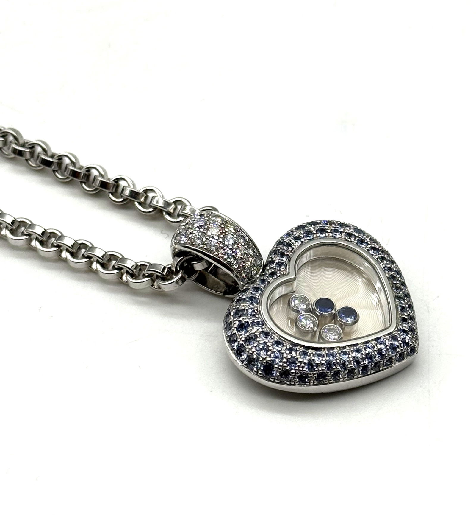 Chopard Happy Diamonds 18K White Gold Heart Pendant Necklace with Diamonds & Sapphires: Authentic Chopard Happy Diamonds heart pendant necklace crafted in 18K white gold. The pendant features Chopard’s signature floating diamonds enclosed within a heart-shaped sapphire crystal, surroun