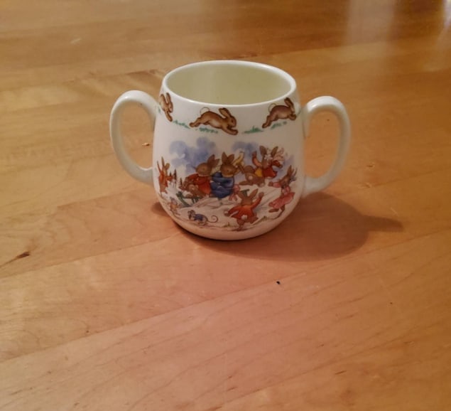 Royal Doulton Bunnykins Double-Handled Cup: Royal Doulton Bunnykins double-handled ceramic cup featuring a colorful scene of rabbits engaged in outdoor activities. The item bears the Royal Doulton hallmark and the Bunnykins logo on the base, de