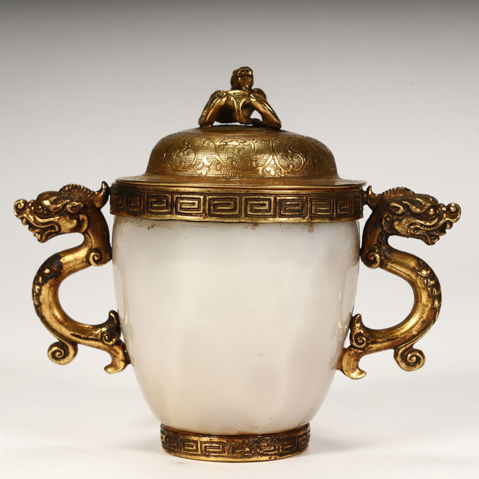 A Tang Dynasty agate gilt double dragon ear cover cup: The agate cup body has a warm and transparent texture, gilt double dragon-shaped ears on both sides, gilded auspicious beasts on the lid, and carved patterns on the lid and cup rim and bottom foot, wi