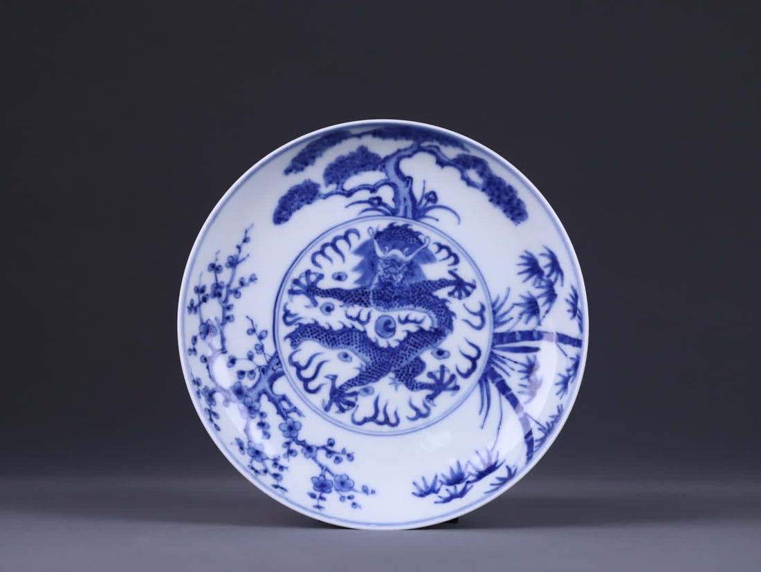 A Qing Dynasty "Qing Guangxu Year System" blue and white pine bamboo plum dragon pattern plate: The Qing Dynasty "Qing Guangxu Year System" blue and white pine bamboo plum dragon pattern plate is a classic official kiln product of the Guangxu period, with a five-clawed dragon in the center, migh