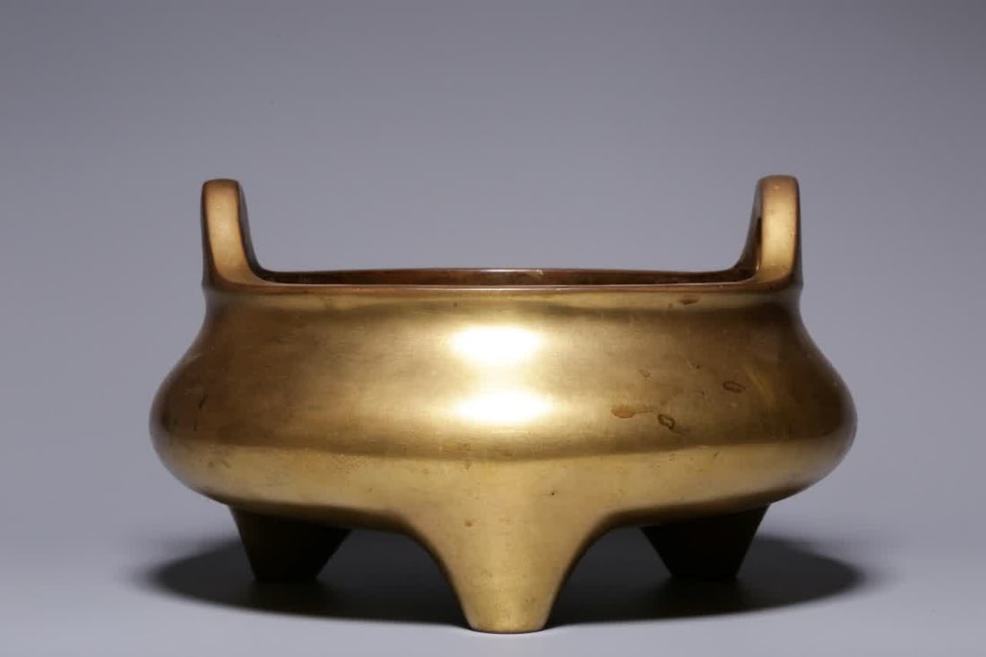 A Qing Dynasty copper gilt bridge ear furnace: Qing Dynasty copper gilt bridge ear furnace This furnace has an open mouth, a short neck, bridge ears, a bulging belly, and a three-legged tripod. The furnace body is well-proportioned, the hall is fu