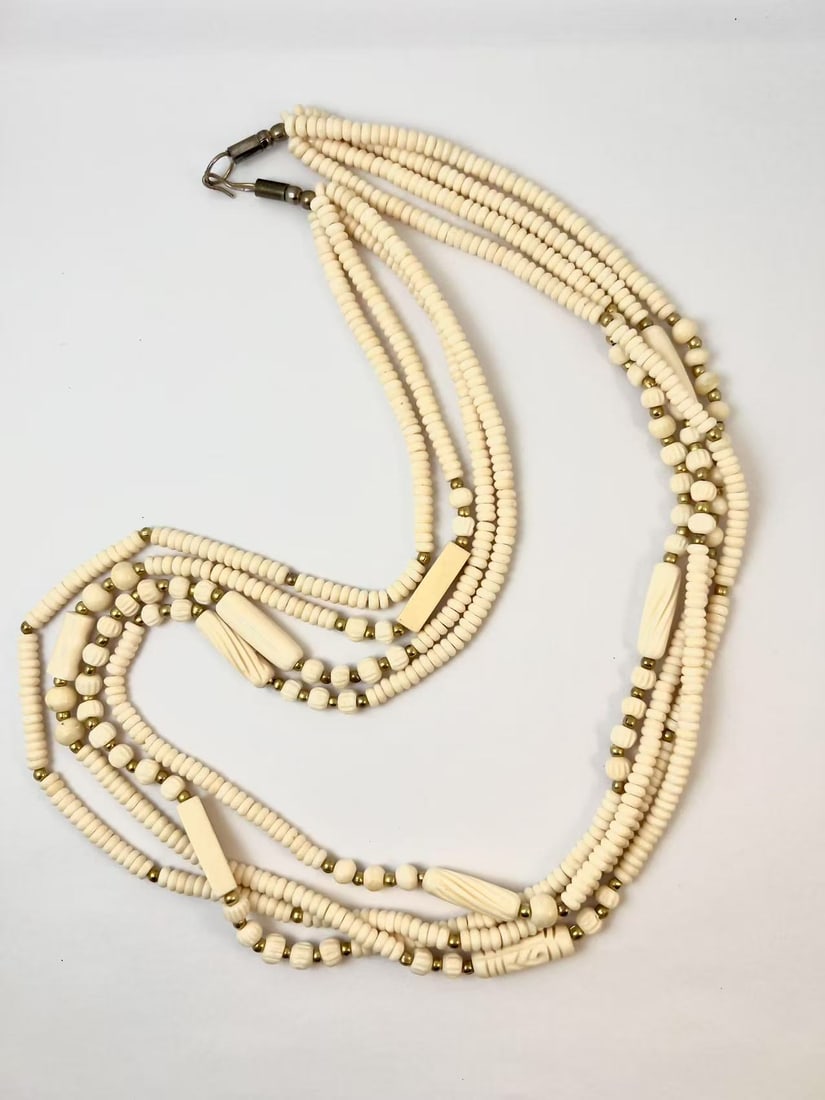 Vintage Multi-Strand Bone Beaded Necklace: A handcrafted vintage multi-strand necklace featuring carved bone beads and small gold-toned spacer beads. The beads vary in shapes and sizes, with some exhibiting hand-carved details. The clasp is a