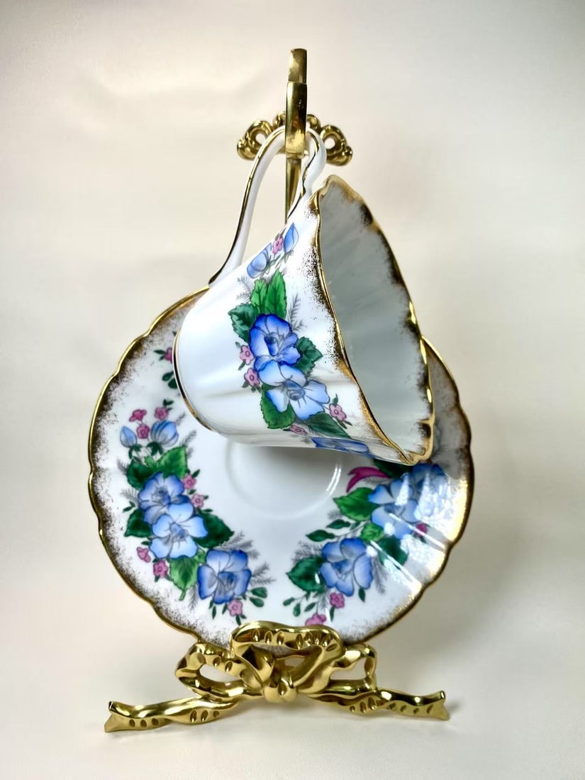 Royal Staffordshire Fine Bone China "Bridal" Blue Floral & Gold Tea Cup and Saucer Set - England: This elegant tea cup and saucer set by Royal Staffordshire Fine Bone China features a charming blue floral motif accented with delicate gold trim. The scalloped edges and intricate detailing add a tou