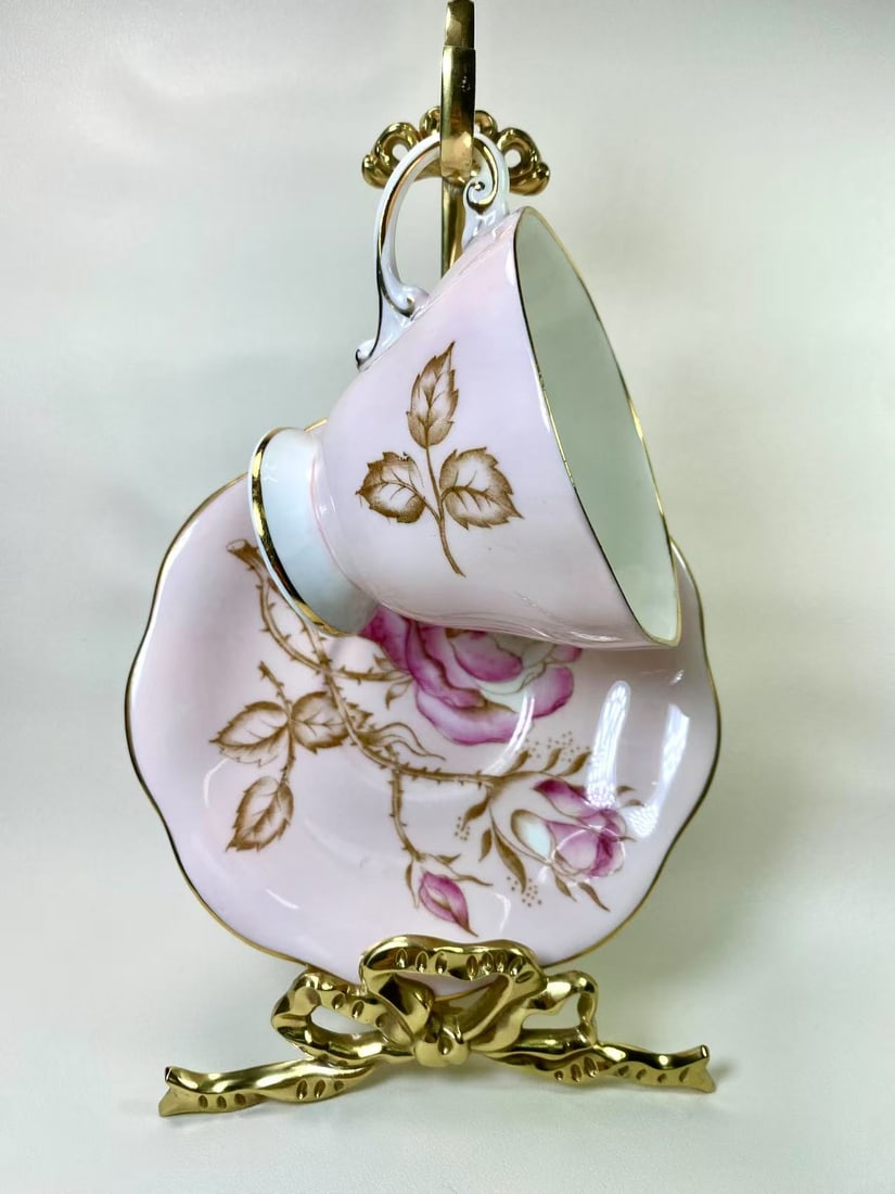 Foley Fine Bone China Pink Rose & Gold Trim Tea Cup and Saucer Set - England: This charming fine bone china tea cup and saucer set by Foley features a soft pink backdrop adorned with hand-painted roses and delicate gold leaf accents. The scalloped edges and gold trim bring a to