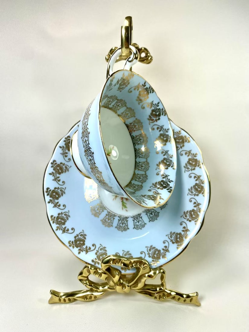 Foley England Pastel Blue and Gold Floral Tea Cup and Saucer Set: A charming tea cup and saucer set by Foley England, adorned with a delicate pastel blue background, intricate gold floral patterns, and a hand-painted flower bouquet at the center. A beautifully craft