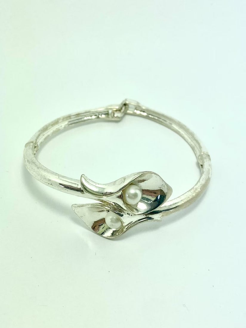 Avon Silver-Tone Calla Lily Hinged Bracelet with Faux Pearls: Vintage hinged bracelet by Avon, crafted with a polished silver-tone finish and adorned with two elegant calla lily flowers embracing faux pearls. Secure clasp design, combining botanical elegance wit