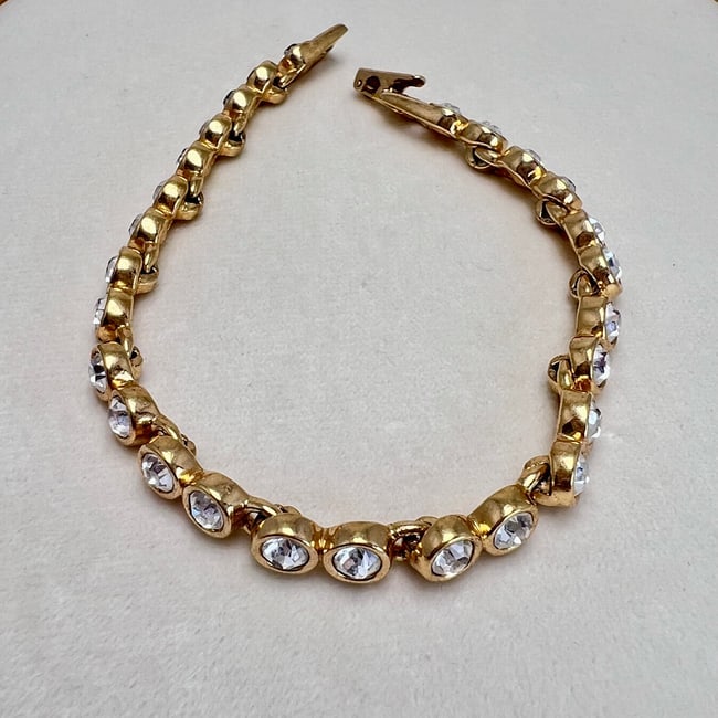 Swarovski Gold-Tone Chain Bracelet with Bezel-Set Crystal Accents: A classic Swarovski chain bracelet featuring a series of bezel-set clear crystals in bright gold-tone metal. Each crystal is securely nestled in a sculpted link, catching the light with every movement