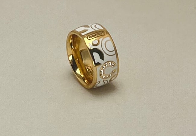 Size 6 Coach Gold-Tone White Enamel Logo Ring with Crystals, Signed: Signed Coach band ring in polished gold-tone metal, overlaid with glossy white enamel and the brand’s signature “C” logo pattern. One “C” is pavé-set with clear crystals for a subtl