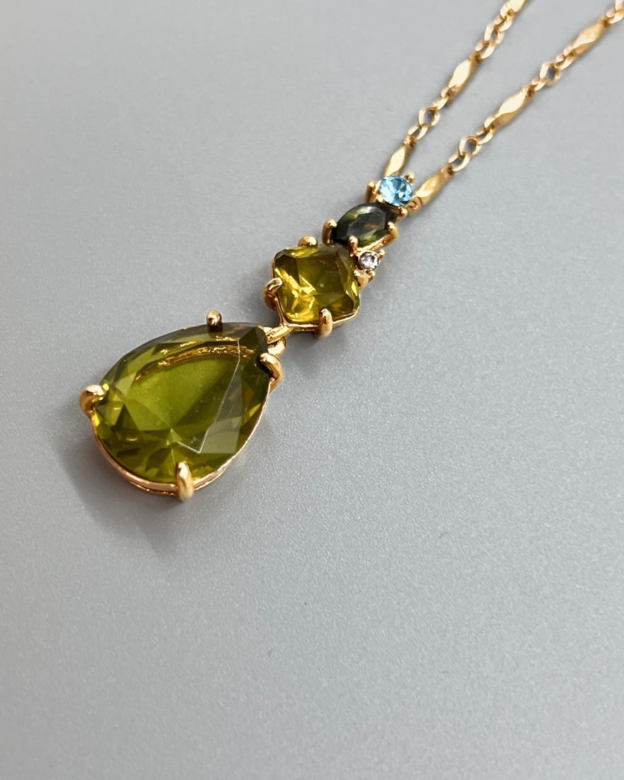 Monet Vintage Gold-Tone Drop Pendant Necklace with Green Glass Stones: A vintage Monet necklace featuring a rich gold-tone textured chain and a dramatic drop pendant set with four faceted glass stones. The pendant showcases a striking olive-green teardrop centerpiece, ac