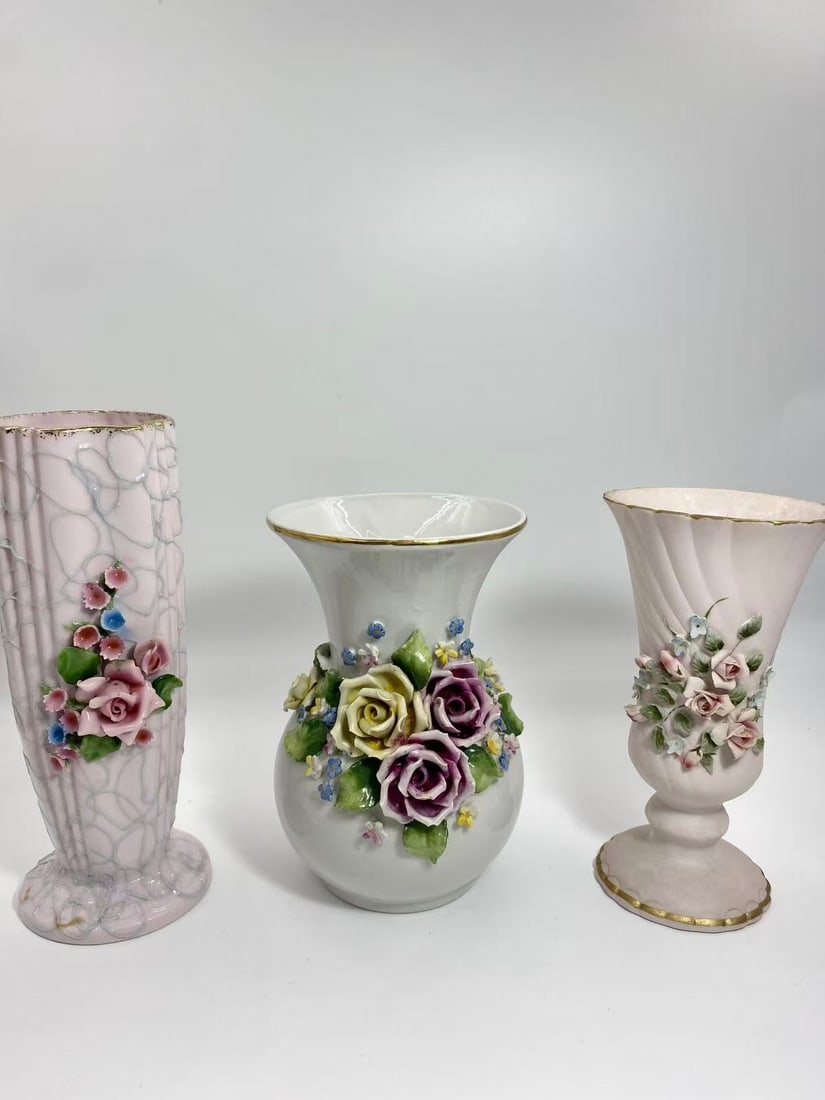Set of 3 Vintage Porcelain Floral Vases _ Japan, Capodimonte Italy, and Handcrafted Rose Bouquet: A charming set of three vintage porcelain vases, featuring finely modeled floral decorations. The collection includes a tall pink vase marked Japan, a white vase richly adorned with colorful roses, an