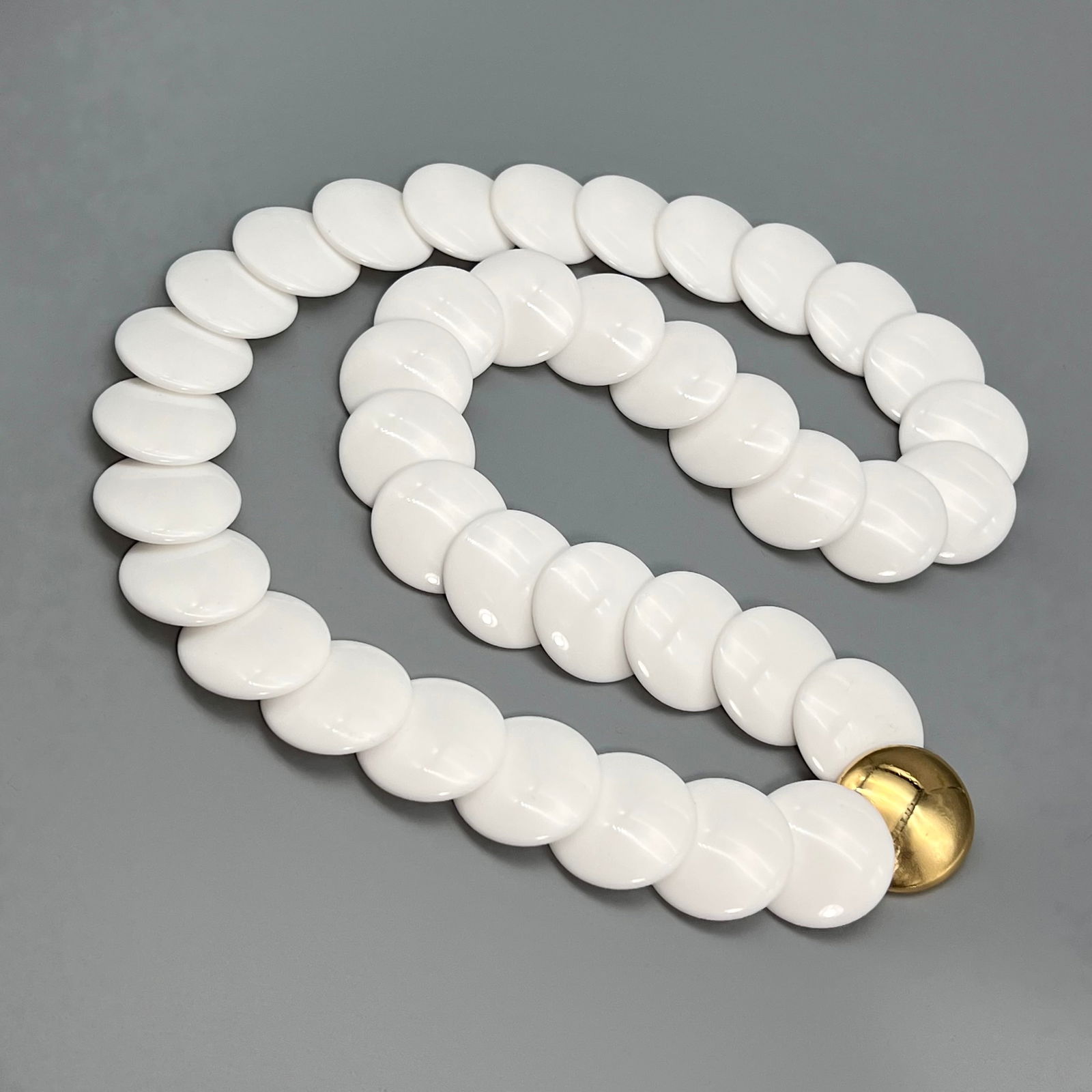 Vintage Trifari White Resin Bead Necklace with Gold Tone Clasp: A bold vintage necklace by Trifari, featuring glossy white resin beads in a smooth, rounded geometric form. The necklace is finished with a statement gold-tone circular clasp, marked TRIFARI on the re