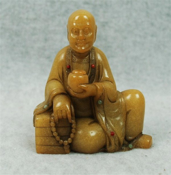 Chinese Tian-Huang Stone Figurine: Chinese tianhuang stone figurine, depicting a louhan (Buddhist worthy) wearing monastic robes and seated in a pose of royal ease, his hands holding an alms bowl and string of rosary beads, the dark ho