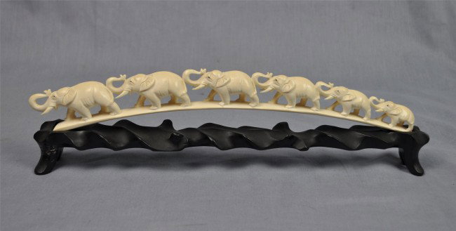 Asian ivory tusk with elephant procession: Asian ivory tusk with elephant procession, 20th century, each of graduated size with trunks raised and walking in single file, the configuration preserving the natural curve of the tusk, with a wooden