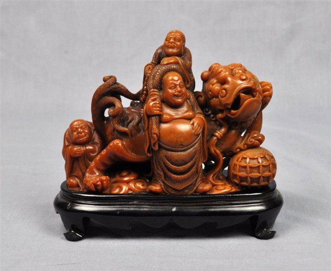 Chinese shoushan stone figural carving: Chinese shoushan stone figural carving, featuring Budai together with other Buddhist sages cavorted with a large fu-lion toying with a brocade ball, the stone of reddish-orange hue with the incised de