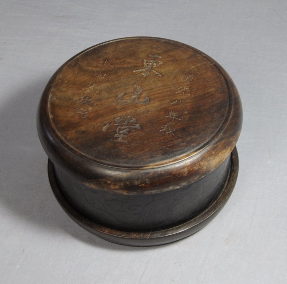 Chinese Carved Round Ink Stone With Wood C: Chinese carved round ink stone with wood cover, decorated with bats and clouds. Early 20th century. 6.25" diam x 2.5" height.