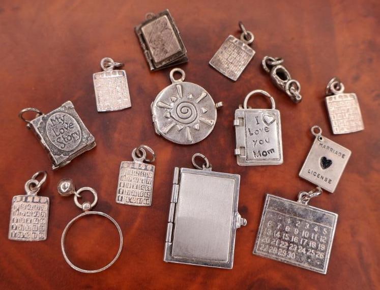 Collection of sterling silver charms: The charms feature various designs, including several book-shaped charms, some of which are likely meant to be engraved. 