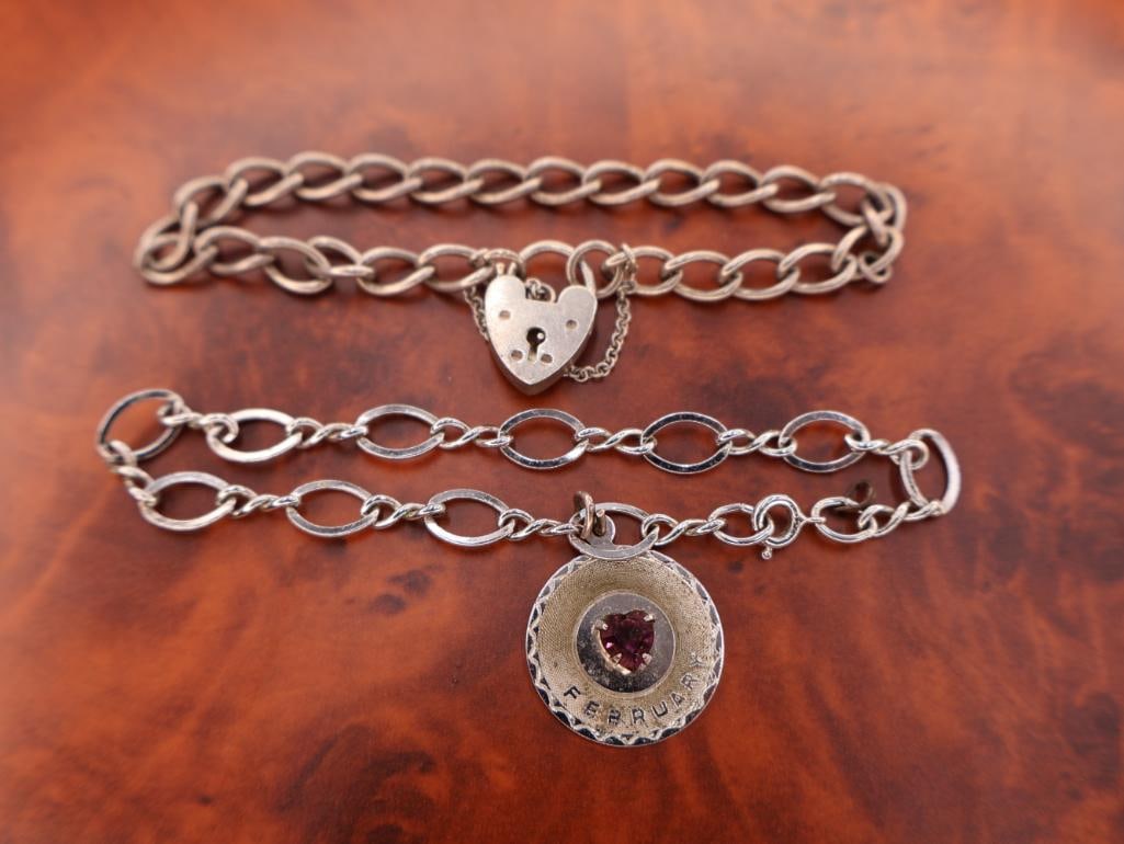 Two sterling silver charm bracelets: These are two sterling silver charm bracelets, one with a heart-shaped padlock clasp and the other with a round "February" birthstone charm. 