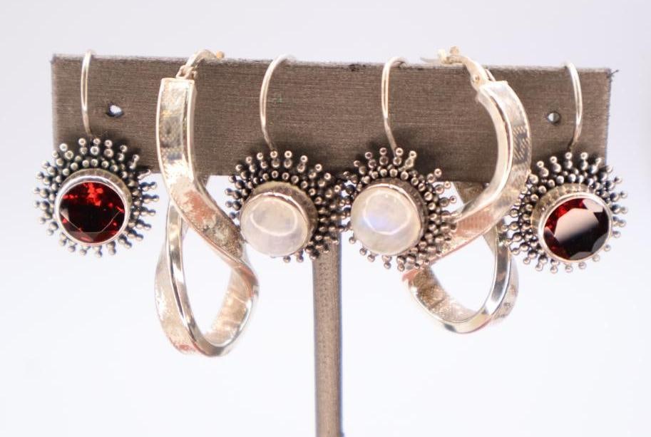Three pairs of sterling silver earrings: Three pairs of sterling silver earrings featuring both red garnet and moonstone gemstones. 