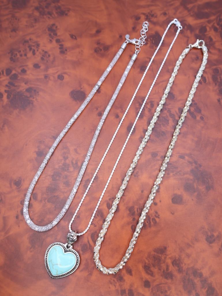 Collection of various silver-tone necklaces: This is a collection of various silver-tone necklaces, including a mesh chain, a delicate link chain, and a turquoise heart pendant necklace. 
