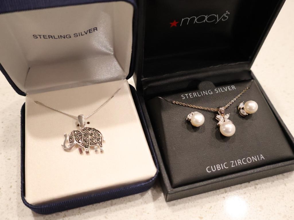 Sterling Silver Pearl & Cubic Zirconia Set and Sterling Silver Marcasite Elephant Necklace: Sterling silver elephant pendant adorned with marcasite stones. Both include original boxes, click on the main photo to view more photos of this lot. The set on the right, from Macy's, includes a