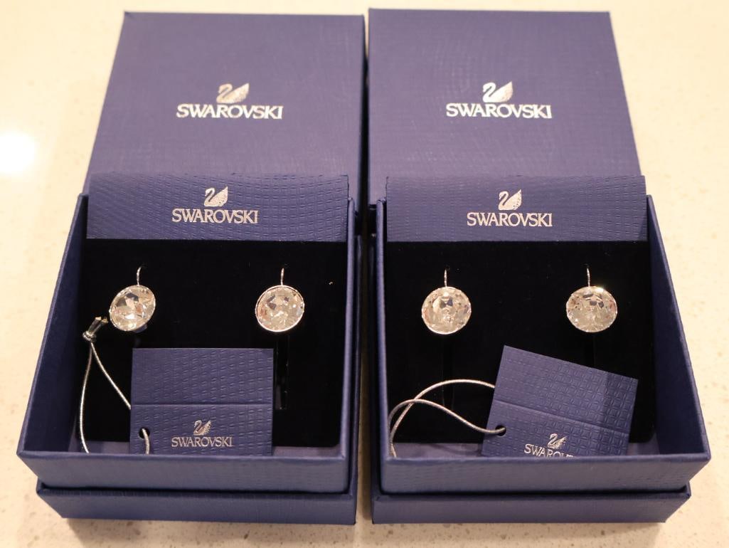 Two pairs of Swarovski Bella Drop Earrings: Each earring features a single, large round-cut clear crystal. The crystals are secured in a bezel setting, which protects the stone and provides a sleek, modern finish. 