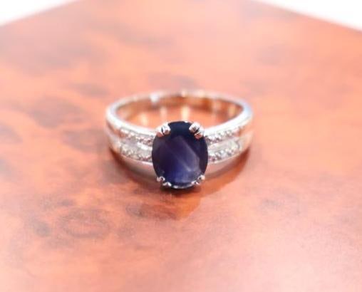 14K White Gold Sapphire and Diamond Ring: Features a prominent oval-cut blue sapphire securely held in a 4-prong setting. The deep navy hue is characteristic of high-quality natural sapphires. 
