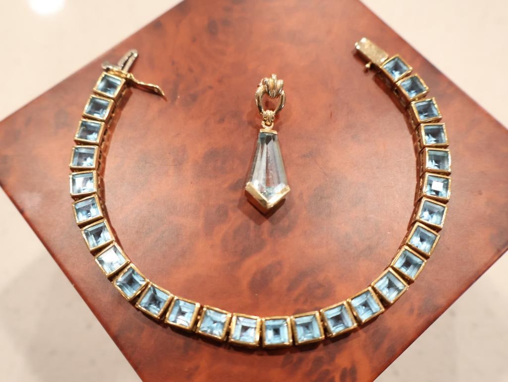 10K Gold Blue Topaz Link Bracelet and Single 14K Gold Blue Topaz Drop Earring: A classic "line" or "tennis" style bracelet consisting of 21 square-cut (princess-cut) blue stones, likely Blue Topaz. An elegant pendeloque or tapered drop earring. It features a large, elongated