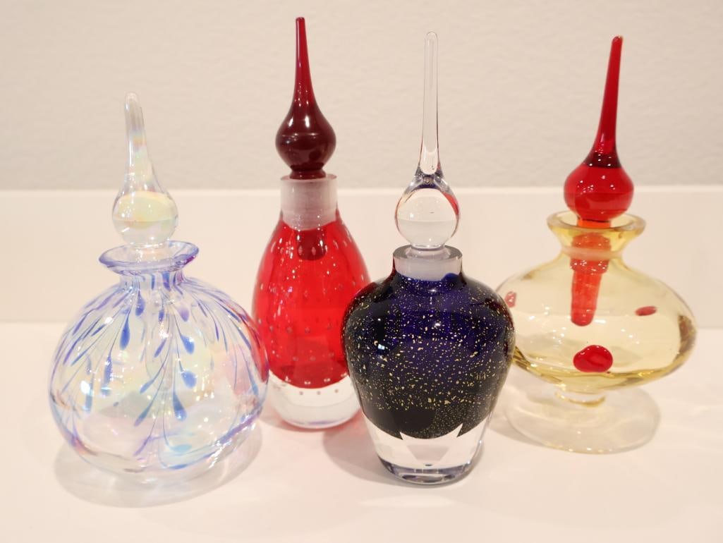 Curated collection of four vintage studio art glass perfume bottles: Each showcasing unique hand-blown techniques and vibrant aesthetics. Iridescent Pulled Feather Bottle, Ruby Red Controlled Bubble Bottle, Flecked "Night Sky" Bottle, Amber Swirl & Gold Bottle. 
