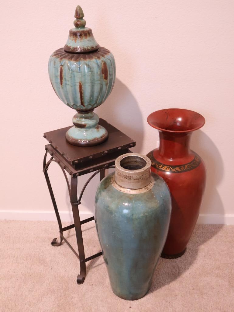 Three decorative ceramic vases and a wrought iron pedestal stand: an Art Deco-style lidded urn featuring a turquoise lustre glaze with deep vertical fluting, a large ovoid-shaped ceramic floor vase with a distinctive "copper-clad" or weathered turquoise patina, a