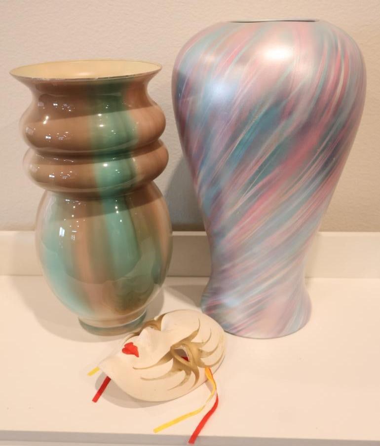 Three decorative items: Two large art glass vases and one hand-painted decorative mask. A large, elegant ceramic or glass vase featuring a dynamic swirling pattern of soft pink, blue, and white hues. A smaller, shapely vase