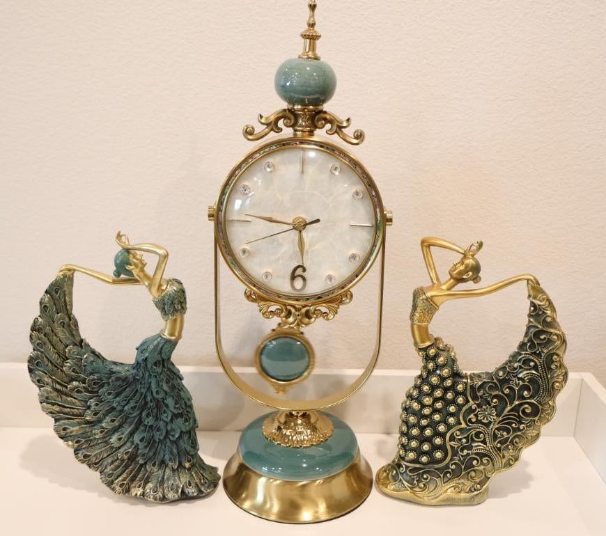 Elegant three-piece decorative set: A luxury vintage-style mantel clock, flanked by two artistic peacock dancer figurines. The centerpiece is a sophisticated Royal Heritage-style table clock. 