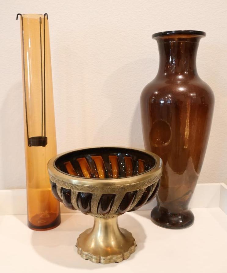 Three decorative glass items representing mid-century modern and Art Deco aesthetics: The center piece is a round pedestal fruit bowl or centerpiece, tall Amber Cylinder Vase, brown Translucent Glass Vase. 