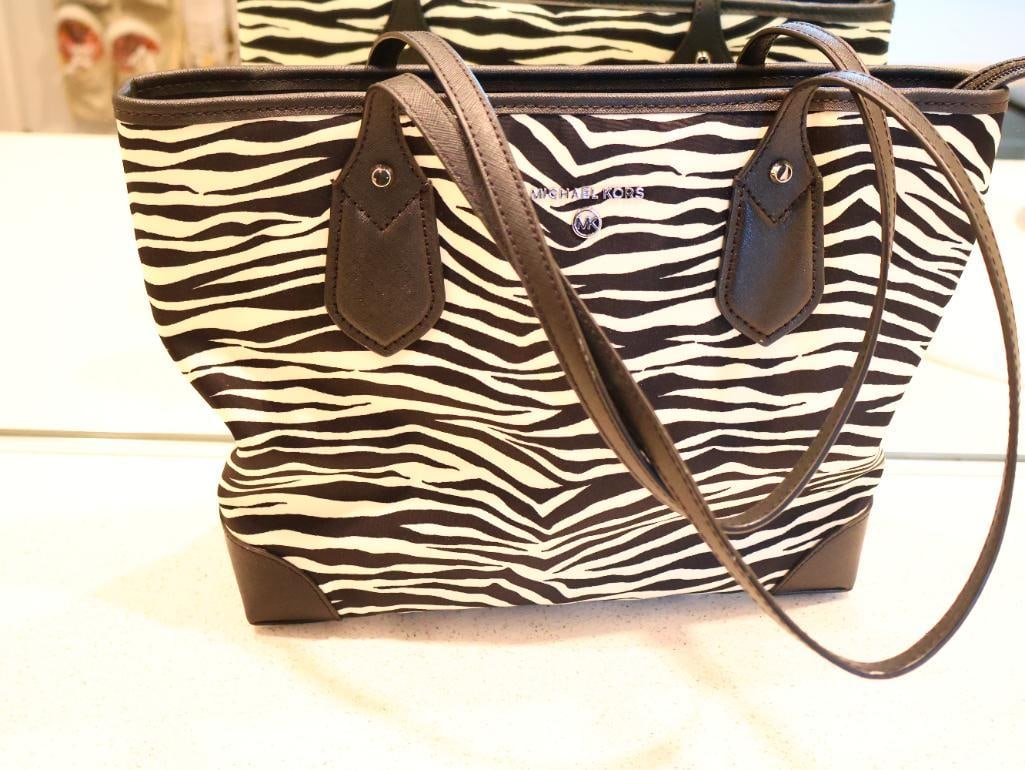 Michael Kors Eva Zebra Top Zip Tote: A structured tote featuring a bold zebra animal print. The body is made of durable and water-resistant nylon, with leather trim and handles. Reinforced leather corners at the base and slim double