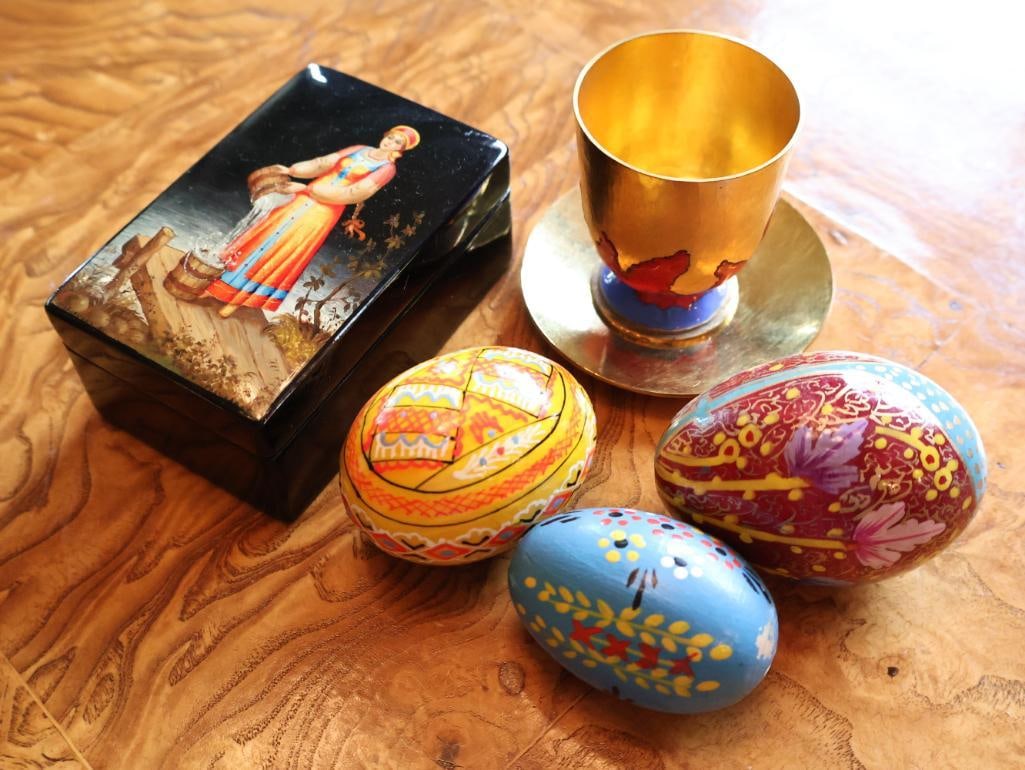 Russian Folk Art Collection Lacquer Box, Hand-Painted Eggs and Enameled Cup: Decorative Russian/Eastern European folk art group featuring a hand-painted black lacquer box with red interior, three colorful painted eggs, and a gold-tone cup and saucer with red and blue enamel