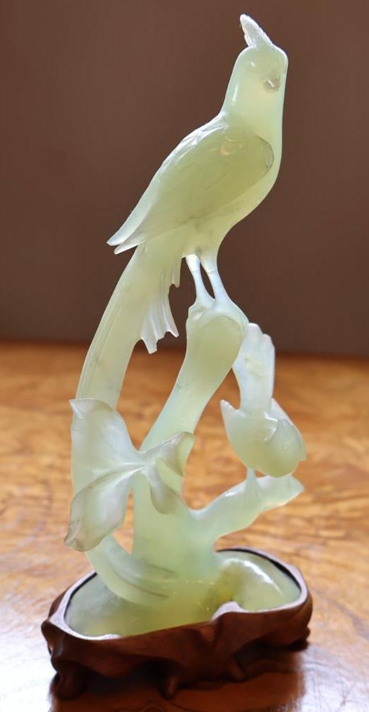 Chinese Carved Pale Green Hardstone Bird & Floral Sculpture on Wood Stand: Finely carved Chinese-style pale green translucent hardstone sculpture depicting a long-tailed bird perched upon flowering branches, with additional blossoms and foliage carved in relief. The stone