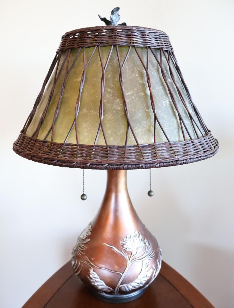 Quoizel Highland 2 Light Table Lamp: Features an organic, soft green oyster mica shade wrapped in a woven wicker overlay. Typically stands around 25 inches tall with a 16.5-inch shade diameter. Topped with a sculpted pine leaf/twig