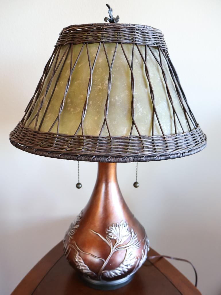 Quoizel Highland 2 Light Table Lamp: Features an organic, soft green oyster mica shade wrapped in a woven wicker overlay. Typically stands around 25 inches tall with a 16.5-inch shade diameter. Topped with a sculpted pine leaf/twig finia